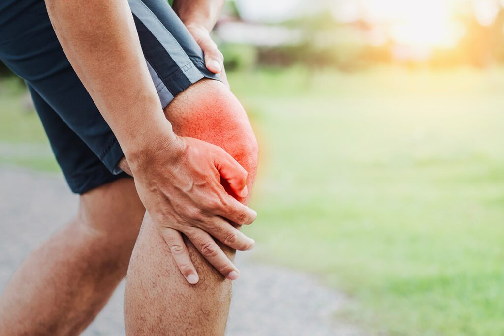 A jogger holding his knee which looks inflamed in pain.