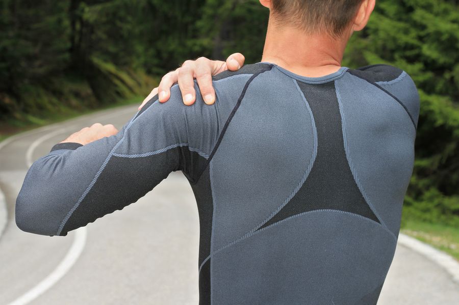 An athletic man in jogging gear trying to relieve the pain in his shoulder by stretching.