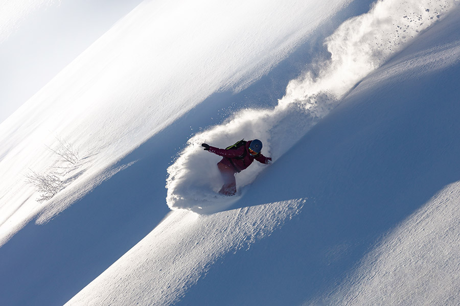 A snowboarder moving steeply downhill on fresh powder.
